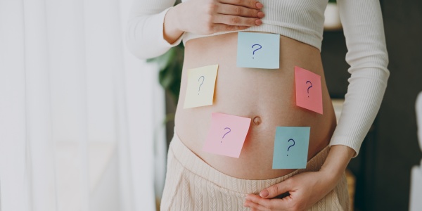 Babybauch voller Post-its mit Fragezeichen.